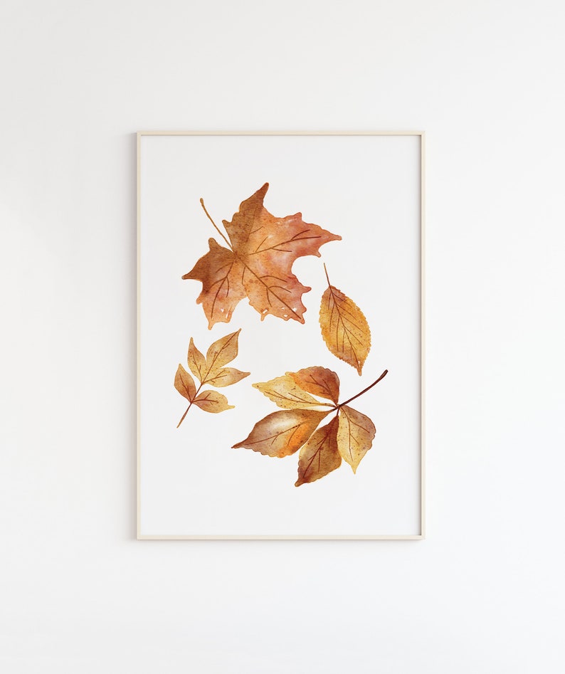 May include: A framed wall art print featuring a watercolor illustration of four autumn leaves in shades of orange, brown, and yellow. The leaves are arranged against a plain white background, showcasing detailed veins and textures in a natural style.