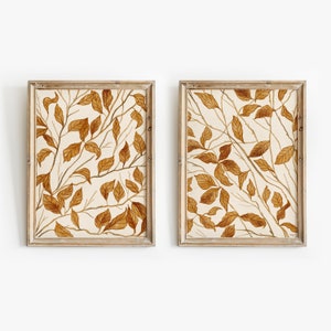 May include: Two framed prints with a beige background and a pattern of brown leaves and branches.