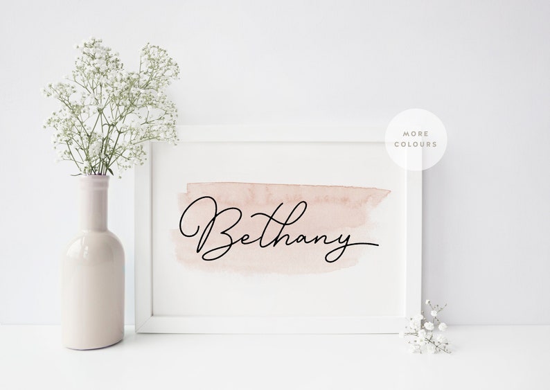Pu&ograve; includere: Una cornice bianca con uno sfondo acquerellato rosa e il nome "Bethany" scritto in corsivo nero. La cornice &egrave; su una superficie bianca con fiori bianchi in un vaso.