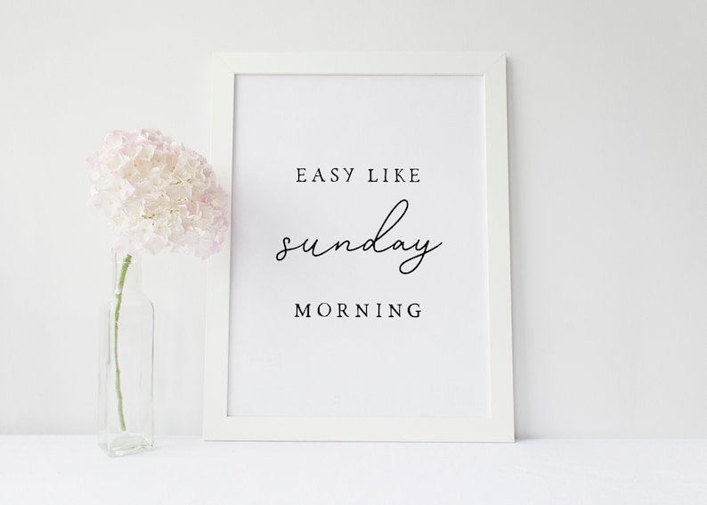 Puede incluir: Impresi&oacute;n enmarcada en blanco con el texto "Easy Like Sunday Morning" en fuente cursiva negra. Una sola hortensia rosa est&aacute; en un jarr&oacute;n de vidrio transparente a la izquierda de la impresi&oacute;n.