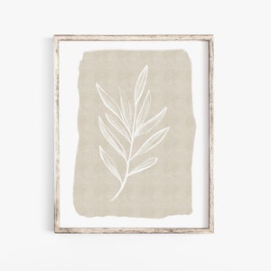 May include: A framed print featuring a beige background with a white line drawing of a branch and leaves.