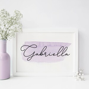 Pu&ograve; includere: Cornice bianca con uno sfondo acquerellato viola e il nome "Gabriella" scritto in corsivo nero.