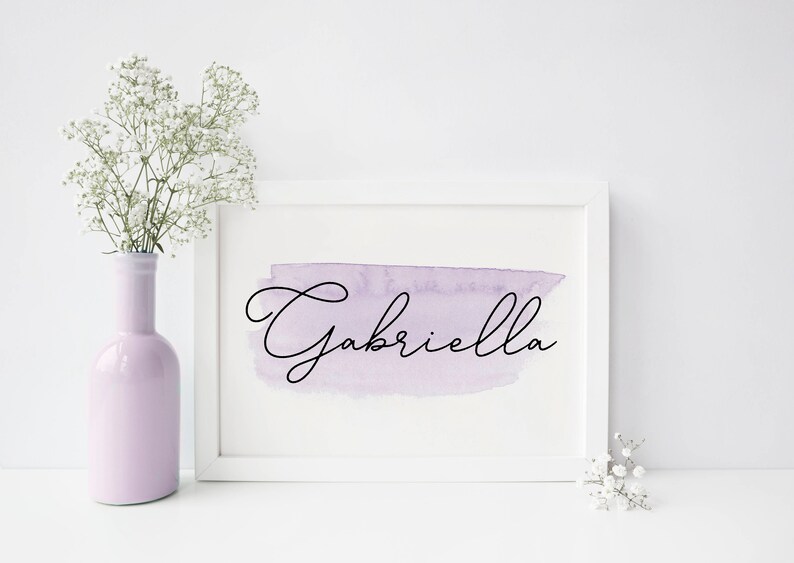 Pu&ograve; includere: Cornice bianca con uno sfondo acquerellato viola e il nome "Gabriella" scritto in corsivo nero.