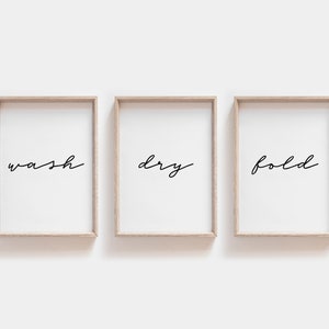 May include: Three wooden framed prints with the words "wash", "dry", and "fold" written in black cursive script.