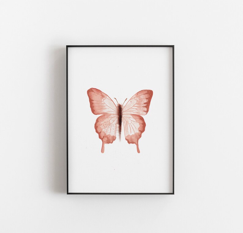 May include: A framed print of a watercolor painting of a butterfly with a light pink color.