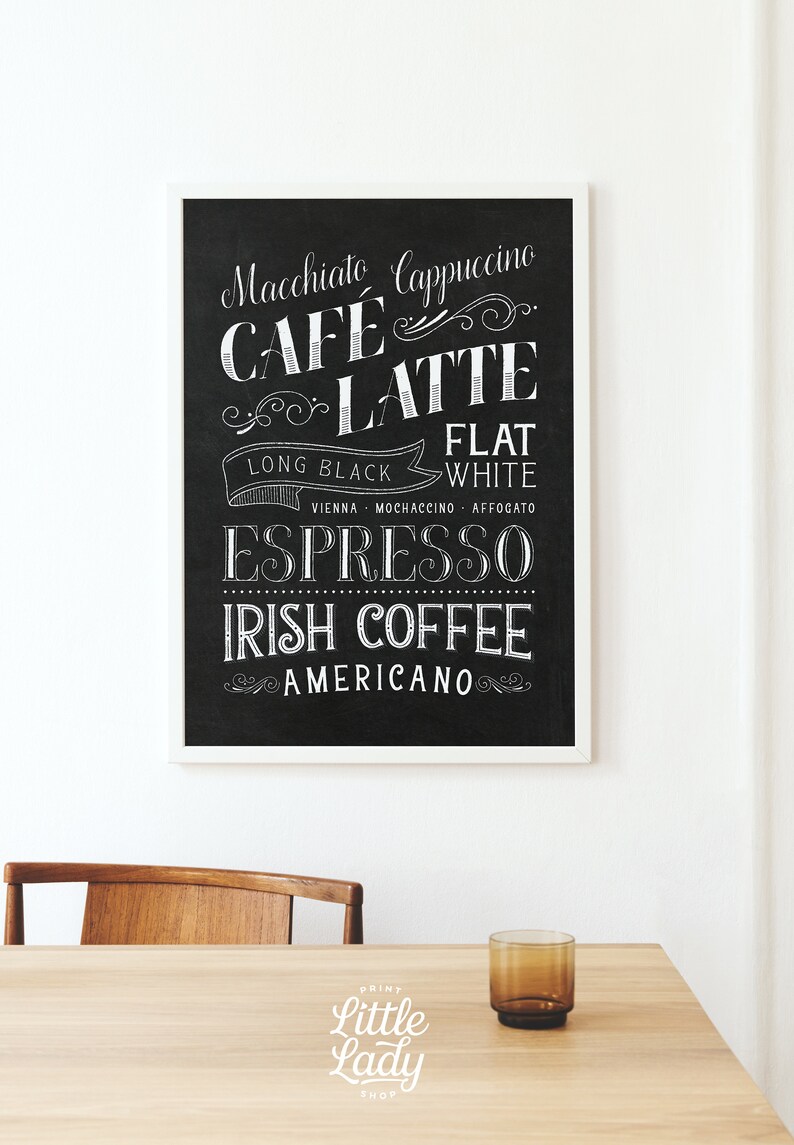 May include: Black and white chalkboard style sign with a white frame listing different types of coffee drinks, including Macchiato, Cappuccino, Cafe Latte, Flat White, Long Black, Vienna, Mochaccino, Affogato, Espresso, Irish Coffee, and Americano. The sign is on a wooden table with a glass of water and a chair.