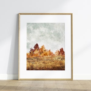 May include: A framed watercolour painting of a landscape with a field of golden brown grass and a line of trees with red, orange, and yellow leaves against a cloudy sky.