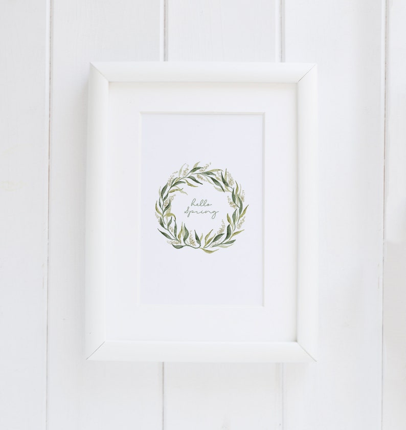 May include: A white framed print with a green and white floral wreath and the text "hello spring" in cursive.