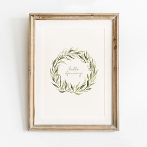 May include: A framed print with a watercolor illustration of a green leafy wreath with white flowers. The wreath surrounds the text "hello spring".
