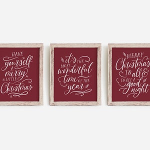 May include: Three framed signs with white calligraphy on a burgundy background. The signs read "Have yourself a merry little Christmas", "It's the most wonderful time of the year", and "Merry Christmas to all & to all a good night".