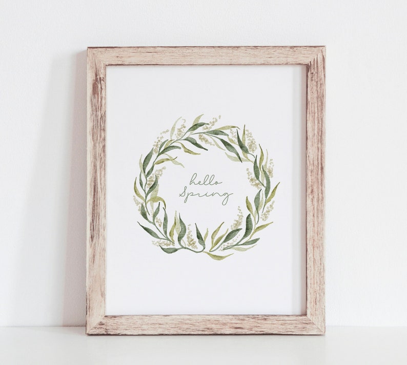 May include: A framed print with a watercolor illustration of a green leafy wreath with the text "hello spring" in the center.