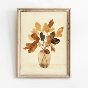 May include: Watercolor painting of a vase with brown leaves. The leaves are various shades of brown and tan, with a few darker leaves. The vase is clear glass. The artwork is framed in a light brown wooden frame.