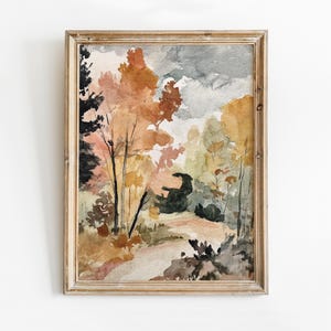 May include: Watercolor painting of a forest scene in a wooden frame. The artwork features trees with orange, yellow, and green foliage, a path, and a cloudy sky. The painting has a soft, muted color palette.