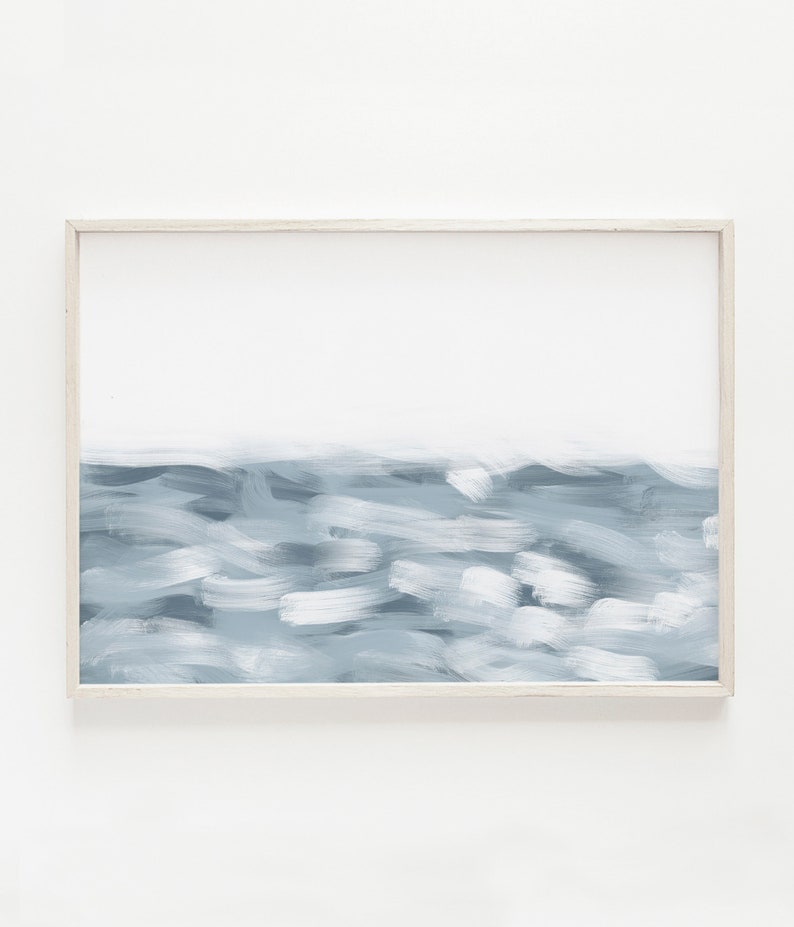 May include: A framed abstract painting of a blue ocean scene with white brushstrokes. The painting is in a white frame and is hanging on a white wall.
