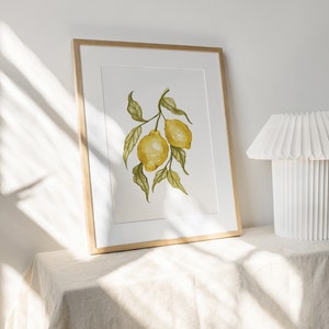 Pode incluir: Uma impress&atilde;o em aquarela emoldurada com dois lim&otilde;es amarelos em um galho com folhas verdes. A obra de arte &eacute; exibida em uma moldura de madeira clara com um passe-partout branco. A impress&atilde;o est&aacute; em uma superf&iacute;cie de cor neutra.