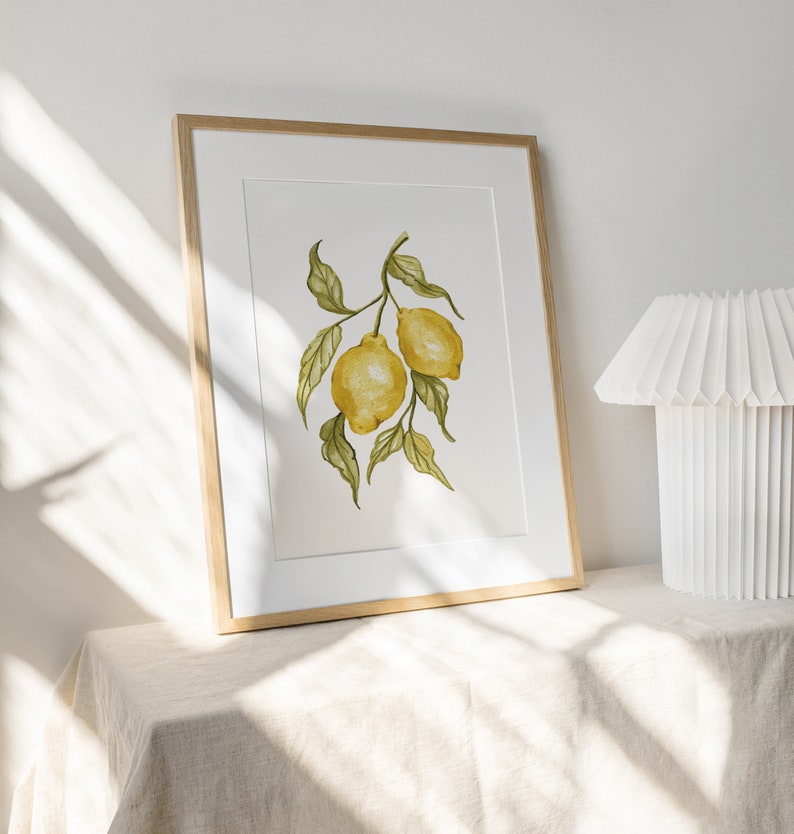 Pode incluir: Uma impress&atilde;o em aquarela emoldurada com dois lim&otilde;es amarelos em um galho com folhas verdes. A obra de arte &eacute; exibida em uma moldura de madeira clara com um passe-partout branco. A impress&atilde;o est&aacute; em uma superf&iacute;cie de cor neutra.