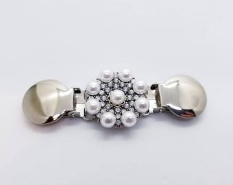 May include: A silver-toned metal clasp with a central floral design. The flower is adorned with white pearls and small clear crystals. The clasp has two rounded ends.