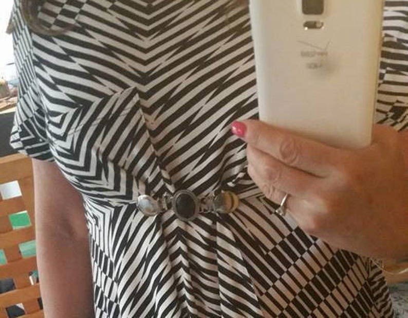 May include: A black and white striped dress with a silver and black belt. The dress has a pocket on the left side.