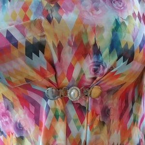 May include: A colorful patterned shirt with a silver and pearl brooch. The shirt has a geometric pattern with pink, yellow, blue, and green colors. The brooch is in the center of the shirt and has a pearl in the center.