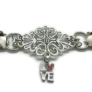 May include: Silver tone decorative clasp with a filigree design and a dangling charm that says "LOVE" with a pink Mickey Mouse head.