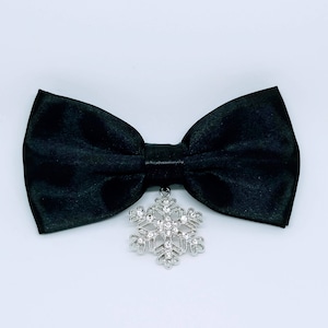 May include: A black satin bow tie with a silver snowflake pendant. The bow tie is made of a smooth, shiny fabric and has a classic shape. The snowflake pendant is detailed with clear crystals.