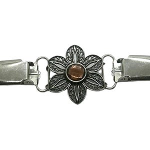 K&ouml;nnte beinhalten: Silberfarbene Metall-Pullover-Clip mit floralem Design. Die Mitte der Blume zeigt einen braunen Edelstein. Der Clip hat an beiden Enden zwei Verschl&uuml;sse, die durch kleine Schlaufen mit der Blume verbunden sind.
