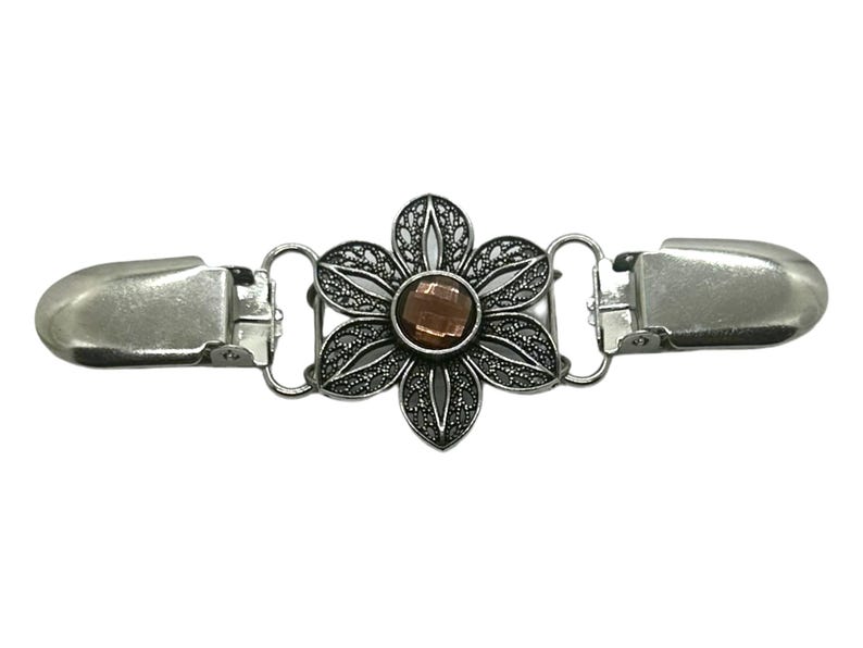 K&ouml;nnte beinhalten: Silberfarbene Metall-Pullover-Clip mit floralem Design. Die Mitte der Blume zeigt einen braunen Edelstein. Der Clip hat an beiden Enden zwei Verschl&uuml;sse, die durch kleine Schlaufen mit der Blume verbunden sind.