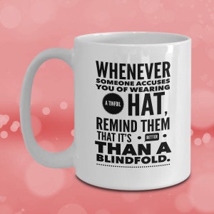 Peut inclure: Une tasse en c&eacute;ramique blanche avec un motif noir qui dit "Whenever someone accuses you of wearing a tinfoil hat, remind them that it's better than a blindfold."
