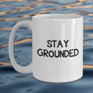 May include: White ceramic coffee mug with a black inscription that reads "STAY GROUNDED".
