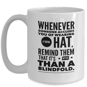 Peut inclure: Une tasse &agrave; caf&eacute; en c&eacute;ramique blanche avec un motif noir qui dit "Whenever someone accuses you of wearing a tinfoil hat, remind them that it's better than a blindfold."