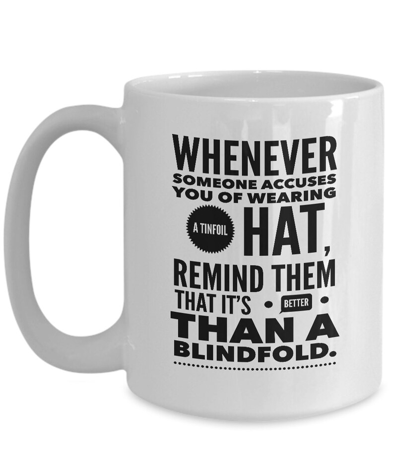 Peut inclure: Une tasse &agrave; caf&eacute; en c&eacute;ramique blanche avec un motif noir qui dit "Whenever someone accuses you of wearing a tinfoil hat, remind them that it's better than a blindfold."