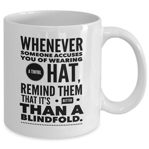 Peut inclure: Une tasse &agrave; caf&eacute; en c&eacute;ramique blanche avec du texte noir qui dit "Whenever someone accuses you of wearing a tinfoil hat, remind them that it's better than a blindfold."