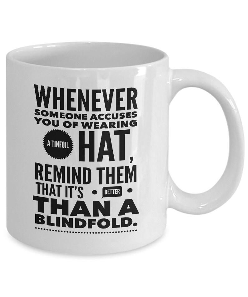 Peut inclure: Une tasse &agrave; caf&eacute; en c&eacute;ramique blanche avec du texte noir qui dit "Whenever someone accuses you of wearing a tinfoil hat, remind them that it's better than a blindfold."