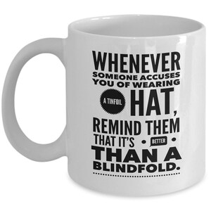 Peut inclure: Une tasse &agrave; caf&eacute; en c&eacute;ramique blanche avec un motif noir qui dit "Whenever someone accuses you of wearing a tinfoil hat, remind them that it's better than a blindfold."
