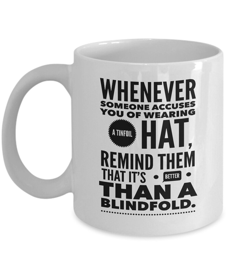 Peut inclure: Une tasse &agrave; caf&eacute; en c&eacute;ramique blanche avec un motif noir qui dit "Whenever someone accuses you of wearing a tinfoil hat, remind them that it's better than a blindfold."