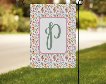 Peut inclure: Un drapeau de jardin blanc avec un motif floral rose et vert. Le drapeau a une bordure rose et une lettre "P" verte au centre.