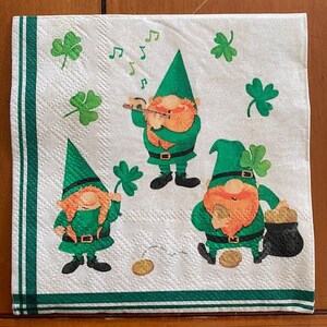 May include: Three green leprechauns with red beards on a white background with green shamrocks. One leprechaun is playing a flute, another is holding a pot of gold, and the third is holding a shamrock.