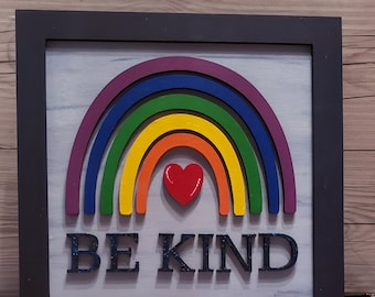 May include: A framed wooden sign with a rainbow design and the words "BE KIND" in black letters. A red heart is in the center of the rainbow.