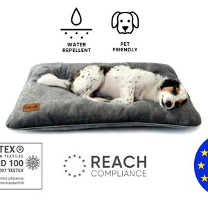 Puede incluir: Una cama para perros gris y blanca con un perro blanco y negro acostado en ella. La cama es repelente al agua y apta para mascotas. La cama est&aacute; hecha en la UE y est&aacute; certificada por Oeko-Tex Standard 100 y REACH.