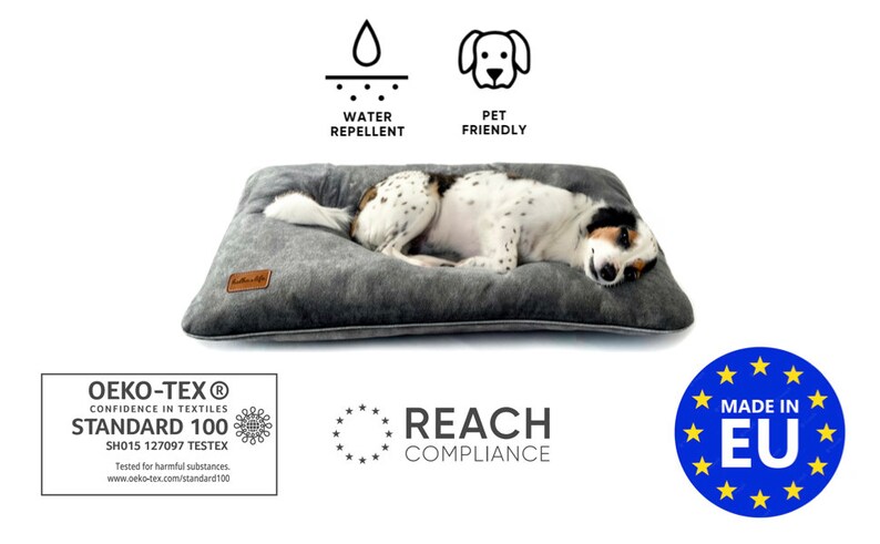 Puede incluir: Una cama para perros gris y blanca con un perro blanco y negro acostado en ella. La cama es repelente al agua y apta para mascotas. La cama est&aacute; hecha en la UE y est&aacute; certificada por Oeko-Tex Standard 100 y REACH.