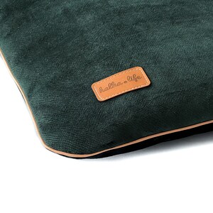 Puede incluir: Una almohada de terciopelo verde oscuro con un parche de cuero marr&oacute;n que dice "halka & life".