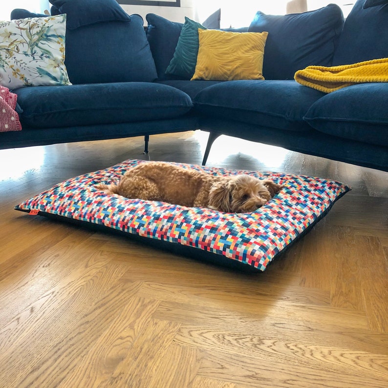 May include: A brown dog sleeping on a colorful patterned dog bed with a black border. The bed is on a wooden floor.