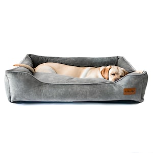 May include: A grey dog bed with a brown dog sleeping in it. The bed has a raised edge and a black base. The bed has a label that says "Rest & Relax".