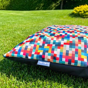 May include: A colorful dog bed with a geometric pattern of squares in various shades of red, blue, yellow, green, and white. The bed has a black border and a "Happy Life" logo.