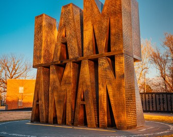 May include: A large, outdoor sculpture made of metal, spelling out the words "I AM A MAN". The sculpture is made of many individual pieces of metal, each with a different inscription. The sculpture is set against a blue sky with a few trees in the background.