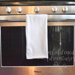 May include: A stainless steel oven with a white kitchen towel hanging on the handle. The oven door is closed and the glass is reflecting the light. The oven has a Whirlpool logo on the bottom.