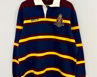 May include: A long-sleeve rugby shirt featuring horizontal stripes in navy blue, burgundy, and yellow. The shirt has a white collar, a button placket, and an embroidered crest on the chest with the text Polo by Ralph Lauren on the neck label.