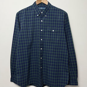 May include: A long-sleeve button-down shirt featuring a dark blue and green plaid pattern. The shirt includes a button-down collar, a single chest pocket with a buttoned flap, and white buttons running down the front placket. The Ralph Lauren logo is visible.