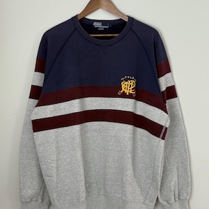 May include: A long-sleeve crewneck sweatshirt featuring a color-blocked design in navy blue, burgundy, and heather gray. The chest displays a yellow embroidered logo with the text Polo and the letters RL intertwined with crossed polo mallets.