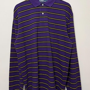 May include: A long-sleeve polo shirt featuring horizontal stripes in purple, black, and yellow. The shirt has a collar, a two-button placket, and a small embroidered logo on the left chest. The interior label reads Polo by Ralph Lauren.